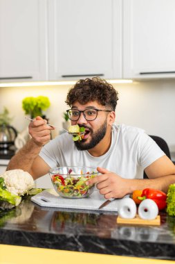 Arap genç adam ev yapımı keto salatasını tadıyor ve kaşıkla yemek yiyor. Sağlıklı beslenme konsepti düşük karbonhidrat sebzelerini ve sağlıklı beslenmek için taze malzemeleri gösterir..
