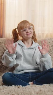 Genç kız mutlu bir gülümsemeyle el sallıyor, neşe ve arkadaşlığı ifade ediyor. Kafkasyalı çocuk bir kanepede oturuyor, merhaba diyor merhaba diyor ya da neşeli ve rahat bir tavırla veda ediyor.