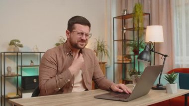 Oturma odasındaki ofis masasında otururken dizüstü bilgisayarı olan Kafkasyalı genç bir işadamı boğaz ağrısı çekiyor. Salgın, salgın, grip, hastalık, test, sağlık, teşhis, koronavirüs.