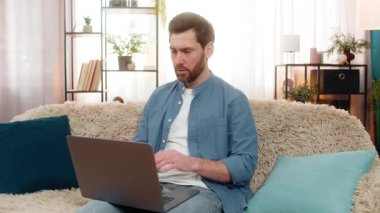 Evde başı dertte olan orta yaşlı bir adam dizüstü bilgisayar ekranına bakarken endişeleniyor. Kanepede oturan beyaz adam, kötü haberlere tepki veriyor ya da hayal kırıklığı ile beklenmedik yüksek harcamalar yapıyor.