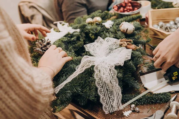 The girl decorates the Christmas wreath with a bow and Christmas toys. Woman making christmas wreath.