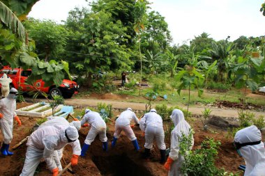 Kamu mezarlığı Pekalongan 'da, 3 Kasım 2020' de kişisel koruma ekipmanlarıyla memurlar tarafından katı sağlık protokolleri uygulanmış 19 hasta için cenaze töreni.