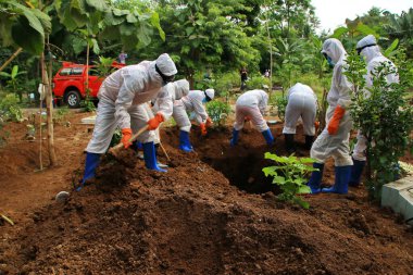 Kamu mezarlığı Pekalongan 'da, 3 Kasım 2020' de kişisel koruma ekipmanlarıyla memurlar tarafından katı sağlık protokolleri uygulanmış 19 hasta için cenaze töreni.