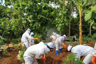 Kamu mezarlığı Pekalongan 'da, 3 Kasım 2020' de kişisel koruma ekipmanlarıyla memurlar tarafından katı sağlık protokolleri uygulanmış 19 hasta için cenaze töreni.
