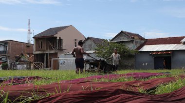 Sıcak bir günde, Pekalongan, Endonezya, 8 Mart 2021 'de tarlada batik kumaş kurutan işçiler.