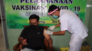 Doktorun elinde şırınga tutması ve pamuk kullanması tıbbi maske Covid-19 veya koronavirüs aşısı, Batang, Endonezya, 15 Mart 2021