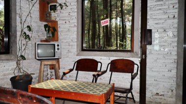 Retro televizyon ahşap taburede, kırsal kafenin içinde. Pencereden orman manzaralı. Nostaljik ve samimi bir atmosfer yaratıyor..