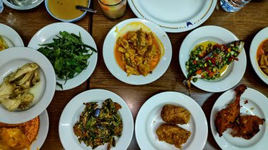 Lokantadaki ahşap bir masada çeşitli lezzetli yemekler sergileniyor, çeşitli lezzetler ve dokular sergileniyor, baştan çıkarıcı bir aşçılık deneyimi yaratıyor..