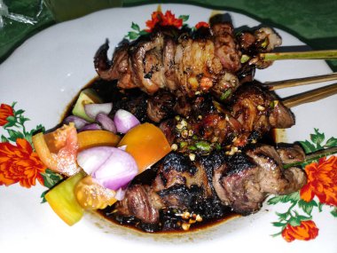 Dekoratif tabakta taze sebze ve baharatlı sosla servis edilen ızgara sığır eti şişleri iştah açıcı ve lezzetli bir mutfak deneyimi yaratıyor..