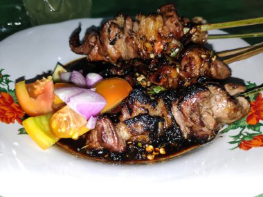 Dekoratif tabakta taze sebze ve baharatlı sosla servis edilen ızgara sığır eti şişleri iştah açıcı ve lezzetli bir mutfak deneyimi yaratıyor..