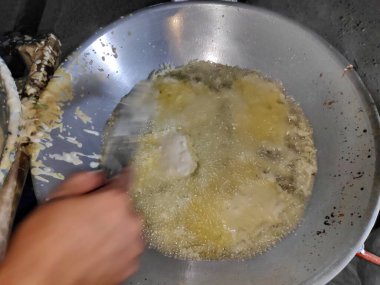Aşçı, geleneksel Endonezya yemeği yapmak için açık mutfakta sıcak yağa hamuru döküyor, canlı ve hareketli bir atmosfer yaratıyor..