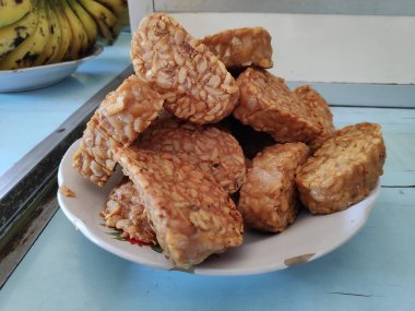 Kızarmış tempeh, beyaz bir tabakta üst üste oturur. Lezzetli ve lezzetli bir aperatif. Keyfini çıkarmaya hazır..