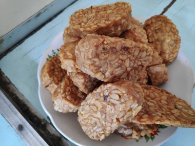 Kızarmış tempeh, beyaz bir tabakta üst üste oturur. Lezzetli ve lezzetli bir aperatif. Keyfini çıkarmaya hazır..