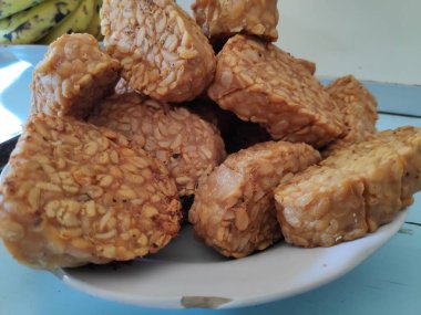 Kızarmış tempeh, beyaz bir tabakta üst üste oturur. Lezzetli ve lezzetli bir aperatif. Keyfini çıkarmaya hazır..