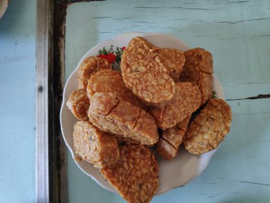 Kızarmış tempeh, beyaz bir tabakta üst üste oturur. Lezzetli ve lezzetli bir aperatif. Keyfini çıkarmaya hazır..