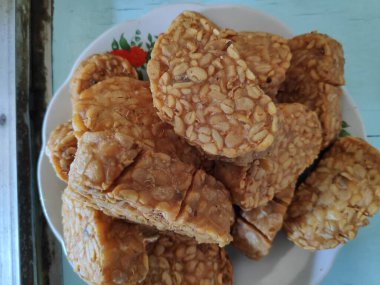 Kızarmış tempeh, beyaz bir tabakta üst üste oturur. Lezzetli ve lezzetli bir aperatif. Keyfini çıkarmaya hazır..