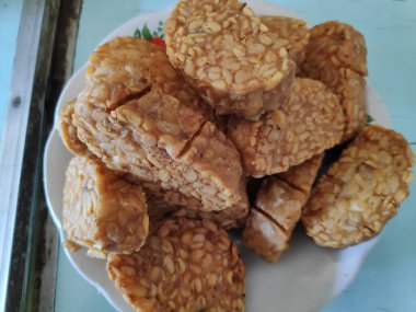 Kızarmış tempeh, beyaz bir tabakta üst üste oturur. Lezzetli ve lezzetli bir aperatif. Keyfini çıkarmaya hazır..