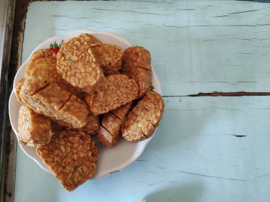 Kızarmış tempeh, beyaz bir tabakta üst üste oturur. Lezzetli ve lezzetli bir aperatif. Keyfini çıkarmaya hazır..