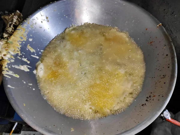 Aşçı, geleneksel Endonezya yemeği yapmak için açık mutfakta sıcak yağa hamuru döküyor, canlı ve hareketli bir atmosfer yaratıyor..