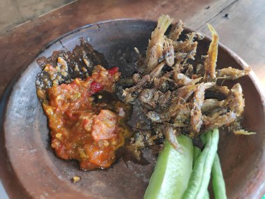 Geleneksel Endonezya yemeği: Kızarmış ançüez, baharatlı sambal ve taze sebzeler otantik yemek pişirme deneyimi için kırsal kilden servis edilir..