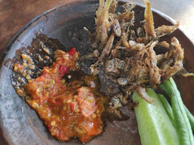 Geleneksel Endonezya yemeği: Kızarmış ançüez, baharatlı sambal ve taze sebzeler otantik yemek pişirme deneyimi için kırsal kilden servis edilir..
