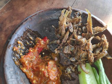 Geleneksel Endonezya yemeği: Kızarmış ançüez, baharatlı sambal ve taze sebzeler otantik yemek pişirme deneyimi için kırsal kilden servis edilir..