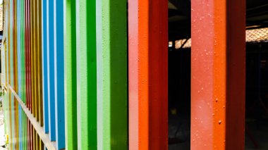 Renkli metal kirişler bir arada durur açık havada canlı bir çit oluşturur, birlik ve yaratıcılık duygusu ile eğlenceli ve modern bir estetik sergiler..