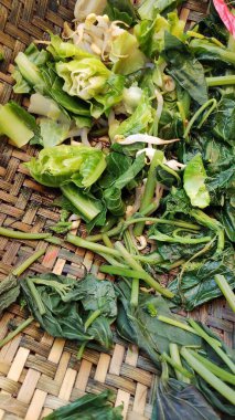 Taze doğranmış yapraklı yeşiller dokunmuş bir sepetin içinde, sade ve besleyici bir yemek haline getirilmeye hazırlar..