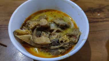 Lezzetli muz körisi ahşap bir masada beyaz bir kasede kaynıyor, sıcak, davetkar bir ışıkta zengin baharatlar ve taze et sergiliyor..