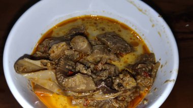 Lezzetli muz körisi ahşap bir masada beyaz bir kasede kaynıyor, sıcak, davetkar bir ışıkta zengin baharatlar ve taze et sergiliyor..