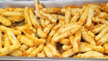 Kalamar dilimlenmiş peynirli çubuklar bir pastanenin metal tepsisinde sergilenir. Altın rengi kabukları ve lezzetli aromalarıyla müşterileri cezbeder..