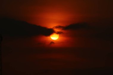 Akşam gökyüzünde, karanlık bulutların ardında parlayan güneş, gün batımında dramatik ve atmosferik bir sahne yaratır..