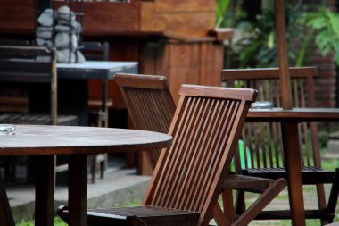 Tahta sandalyeler ve masalar verimli yeşilliklerle çevrili bir verandada huzur içinde otururlar. Sakin bir ortamda rahatlatıcı bir açık hava yemek alanı yaratırlar.
