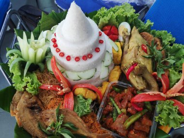 Geleneksel Endonezya yemeği olan Tumpeng pilavı, muz yapraklarıyla kaplı bir sepette çeşitli mezeler ve sebzelerle servis edilir..