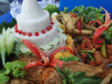 Tumpeng pilavı, geleneksel koni biçimli pirinç tabağı, muz yapraklarıyla kaplı bir septte çeşitli mezeler ve sebzelerle servis edilir..