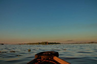 Güneş, mavi okyanus ve yaz gölü bulutlarının ufkunun altına batarken sakin deniz ve nehir manzarasına güzel bir turuncu gün batımı yansıyor.