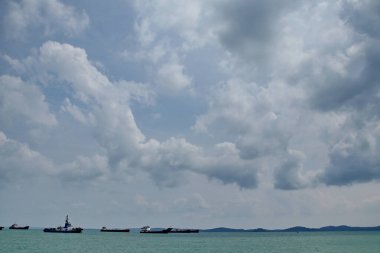 A fishing boat and cargo vessel navigate the blue ocean water under a cloudy sky as industrial shipping tankers transport freight through the deep sea landscape