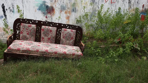 Soluk desenli yastıkları olan terk edilmiş eski bir kanepe, beton bir duvarın yanındaki çimlerin üzerinde duruyor. Şehir çürümesini doğayla harmanlıyor, unutulmuş alanları geri alıyor..