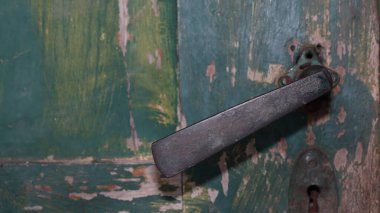 Çürümüş yeşil ahşap kapı, kabuk soyan boya, kırsal doku ve görünür bir anahtar deliği olan antika metal kol. Unutulmuş, eski bir atmosferi çağrıştırıyor..