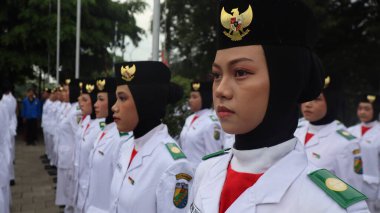 Endonezyalı genç kadınlar, 2 Haziran 2025 'te Paskribaka, Pekalongan, Endonezya, Paskribaka, Pekalongan, Endonezya gibi resmi bir törene katılan, ulusal amblemle süslenmiş siyah bereliler ve başörtüleri takıyorlar.