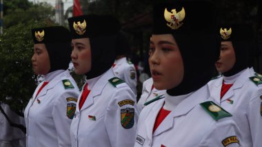 Endonezyalı genç kadınlar, 2 Haziran 2025 'te Paskribaka, Pekalongan, Endonezya, Paskribaka, Pekalongan, Endonezya gibi resmi bir törene katılan, ulusal amblemle süslenmiş siyah bereliler ve başörtüleri takıyorlar.