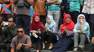 Bir grup insan bir parkta çimlerin üzerinde oturuyor. Rahatlıyorlar ve 14 Ağustos 2025 'te Pekalongan Endonezya' da bir gösteri veya yarışma izliyorlar.