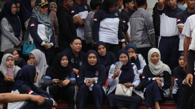 Bir grup insan bir parkta çimlerin üzerinde oturuyor. Rahatlıyorlar ve 14 Ağustos 2025 'te Pekalongan Endonezya' da bir gösteri veya yarışma izliyorlar.