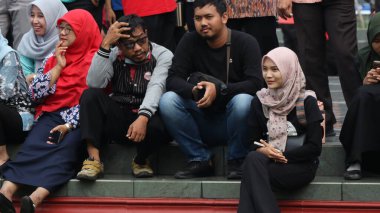 Bir grup insan bankta oturuyor, biri gülüyor. Sahne neşeli ve dost canlısı, Pekalongan Endonezya, 14 Ağustos 2025