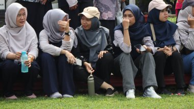 Bir grup insan bankta oturuyor, biri gülüyor. Sahne neşeli ve dost canlısı, Pekalongan Endonezya, 14 Ağustos 2025