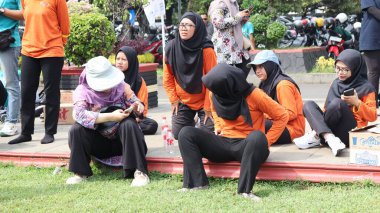 Bir grup insan bankta oturuyor, biri gülüyor. Sahne neşeli ve dost canlısı, Pekalongan Endonezya, 14 Ağustos 2025