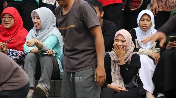 Bir grup insan bir parkta çimlerin üzerinde oturuyor. Rahatlıyorlar ve 14 Ağustos 2025 'te Pekalongan Endonezya' da bir gösteri veya yarışma izliyorlar.