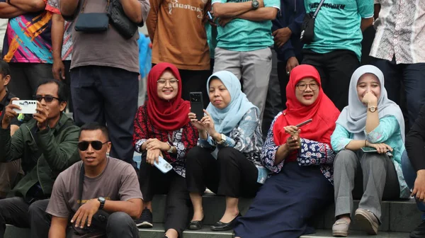 Bir grup insan bir parkta çimlerin üzerinde oturuyor. Rahatlıyorlar ve 14 Ağustos 2025 'te Pekalongan Endonezya' da bir gösteri veya yarışma izliyorlar.