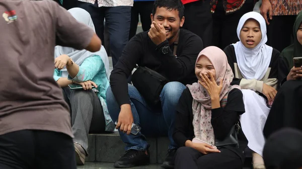 Bir grup insan bankta oturuyor, biri gülüyor. Sahne neşeli ve dost canlısı, Pekalongan Endonezya, 14 Ağustos 2025