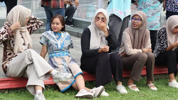 Bir grup insan bankta oturuyor, biri gülüyor. Sahne neşeli ve dost canlısı, Pekalongan Endonezya, 14 Ağustos 2025